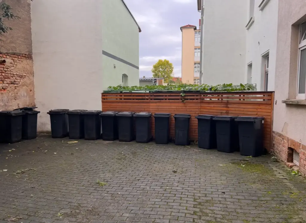 Mülltonnenbereitstellung: viele schwarze Mülltonnen in einer Hofeinfahrt